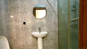 A bathroom with a toilet, a pedestal sink, and a glass shower enclosure. - Serviced Apartment (Lekki)