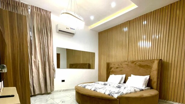 A modern bedroom with a round bed, marble flooring, wooden paneling, and recessed lighting. - Serviced Apartment (Lekki)