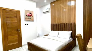 A modern bedroom with a bed, a wooden door, a framed picture, and a ceiling light fixture. - Serviced Apartment (Lekki)