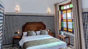 A bedroom with a large bed, a wooden headboard, a patterned floor, a window with curtains, and a hanging light fixture. - Riad Al Mozyane (Fès)