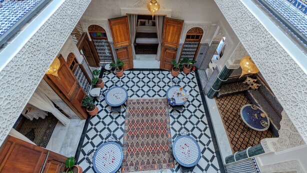 A courtyard with a patterned floor, wooden furniture, and potted plants. - Riad Al Mozyane (Fès)