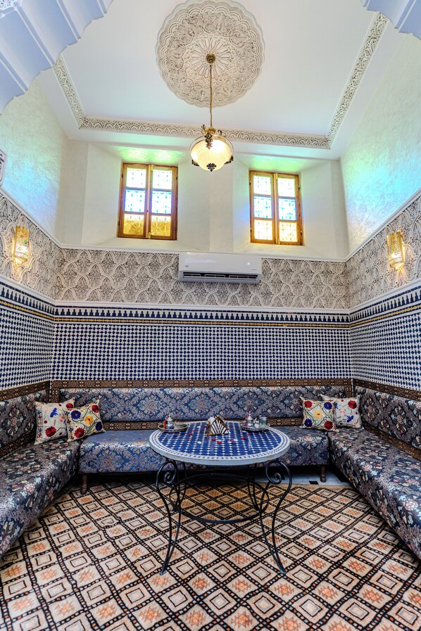 A room with a patterned floor, a sofa set, a round table, and a decorative ceiling. - Riad Al Mozyane (Fès)