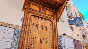 A large wooden door with a metal latch, set in a building with a tiled base and a small window above. - Riad Al Mozyane (Fès)