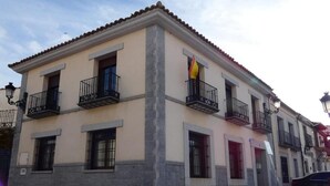 Un immeuble à deux étages, doté de balcons, d’un drapeau et d’une voiture garée.