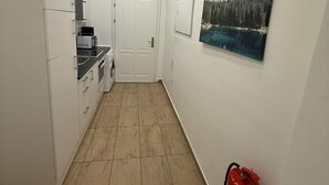 Un couloir étroit avec un coin cuisine sur la gauche, une porte au fond et un extincteur sur la droite.