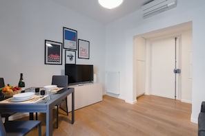 Una sala de estar moderna con comedor, paredes blancas, un televisor de pantalla plana, cuadros enmarcados y un radiador.