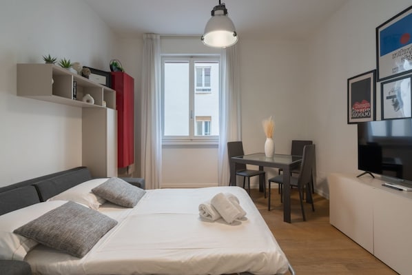 Una habitación de hotel moderna con una cama, un escritorio, una silla, un televisor y una ventana con cortinas.
