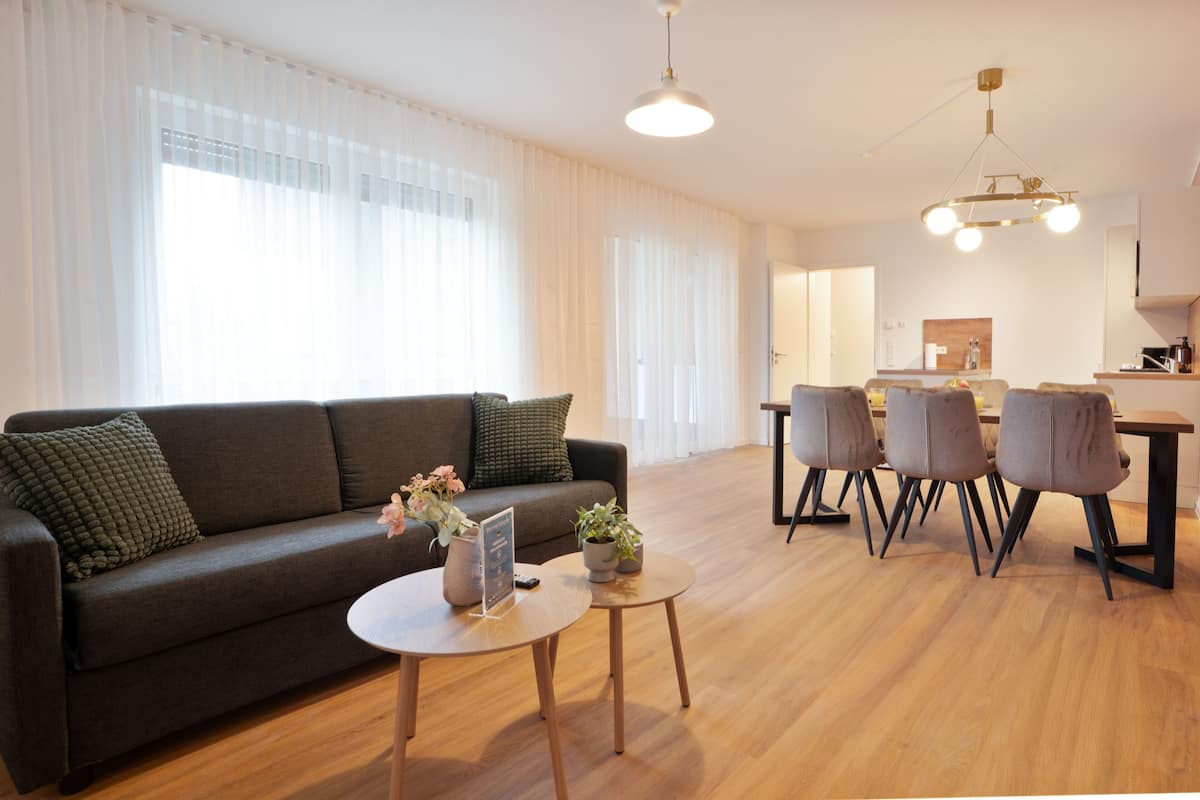 A modern living room with a dark sofa, a round coffee table, and a dining area with chairs and a table.
