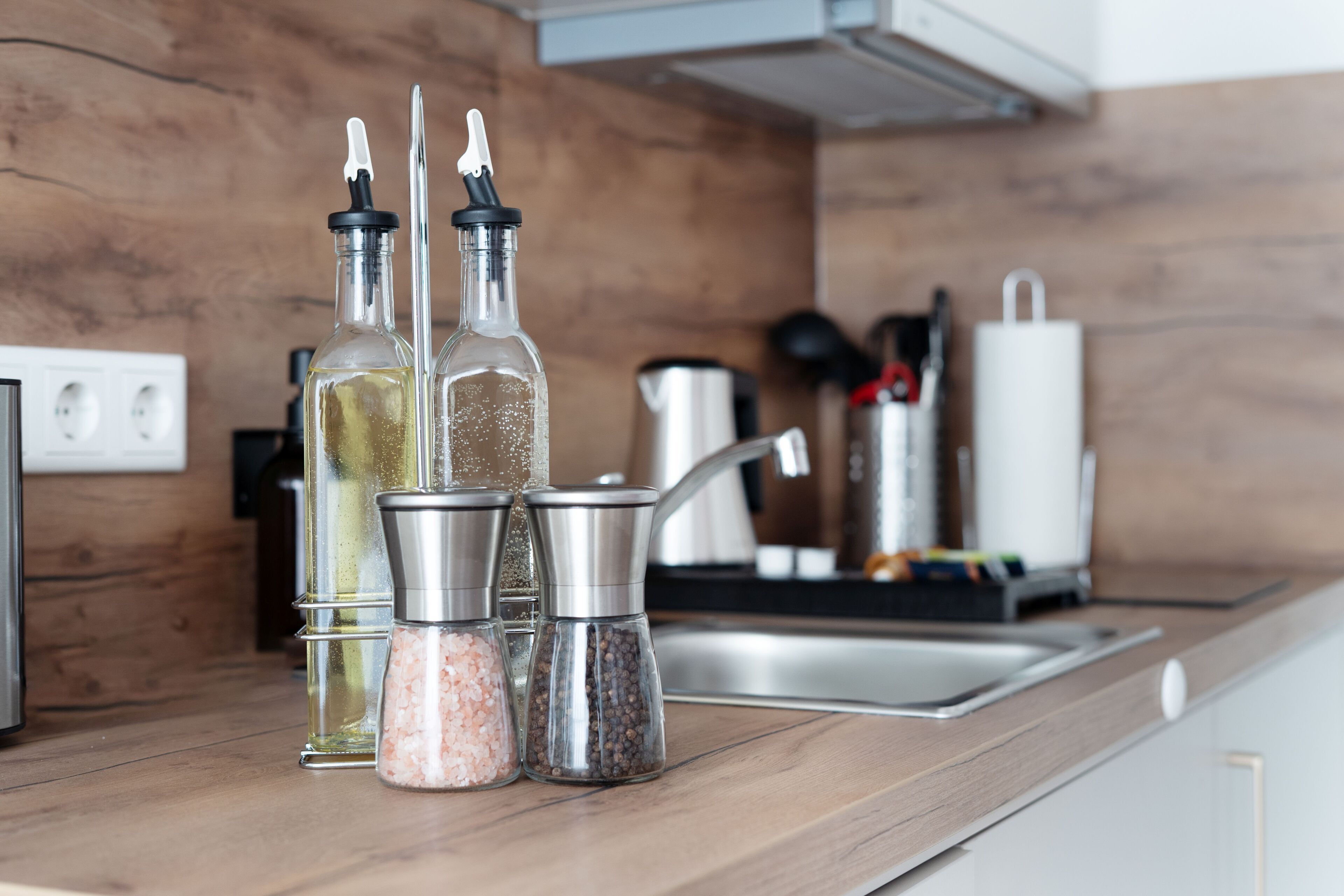 Una encimera de cocina con saleros y pimenteros, una botella de aceite de oliva y una cafetera.