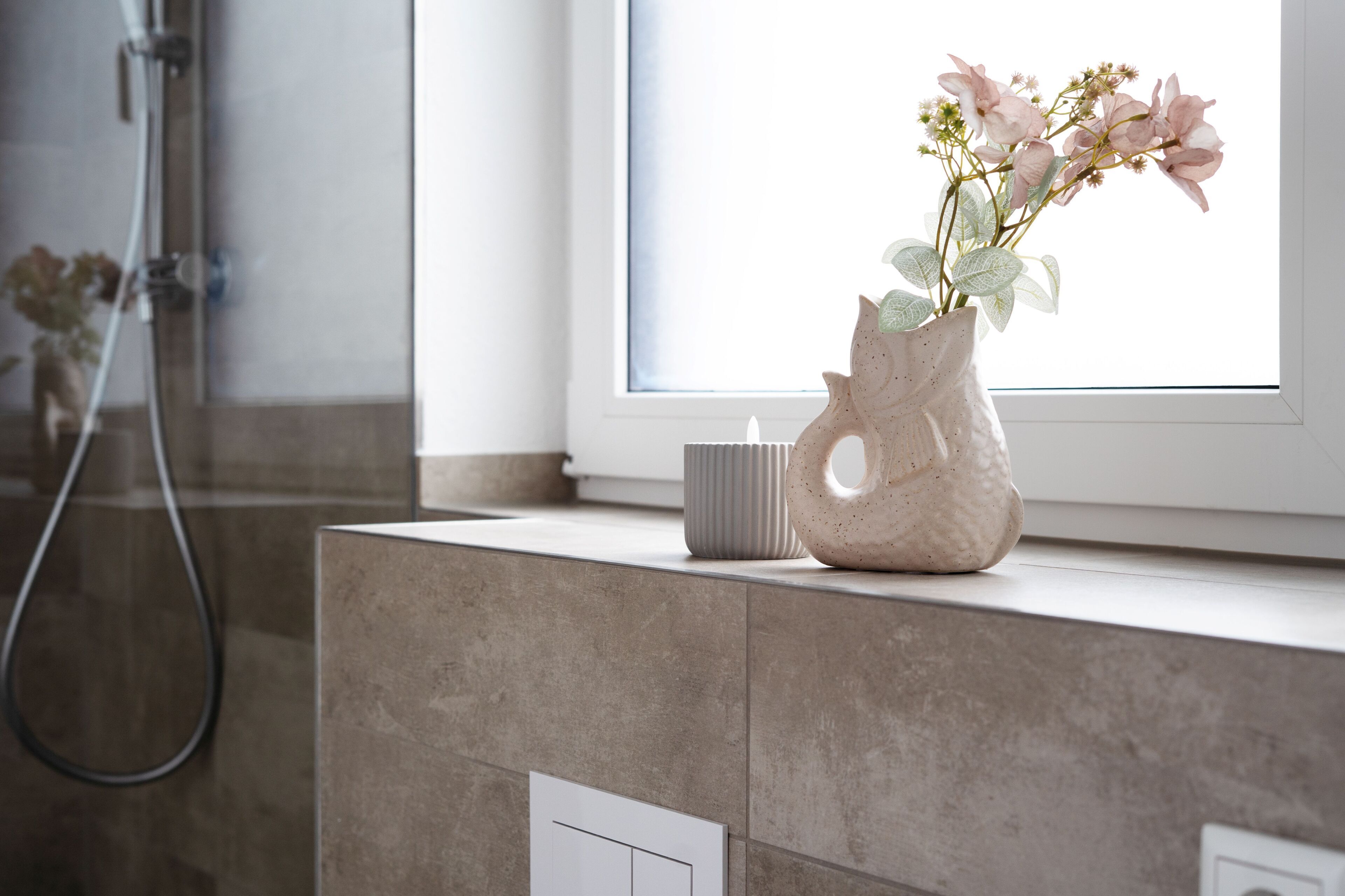 A bathroom with a shower, a window, and a vase with flowers on a counter.