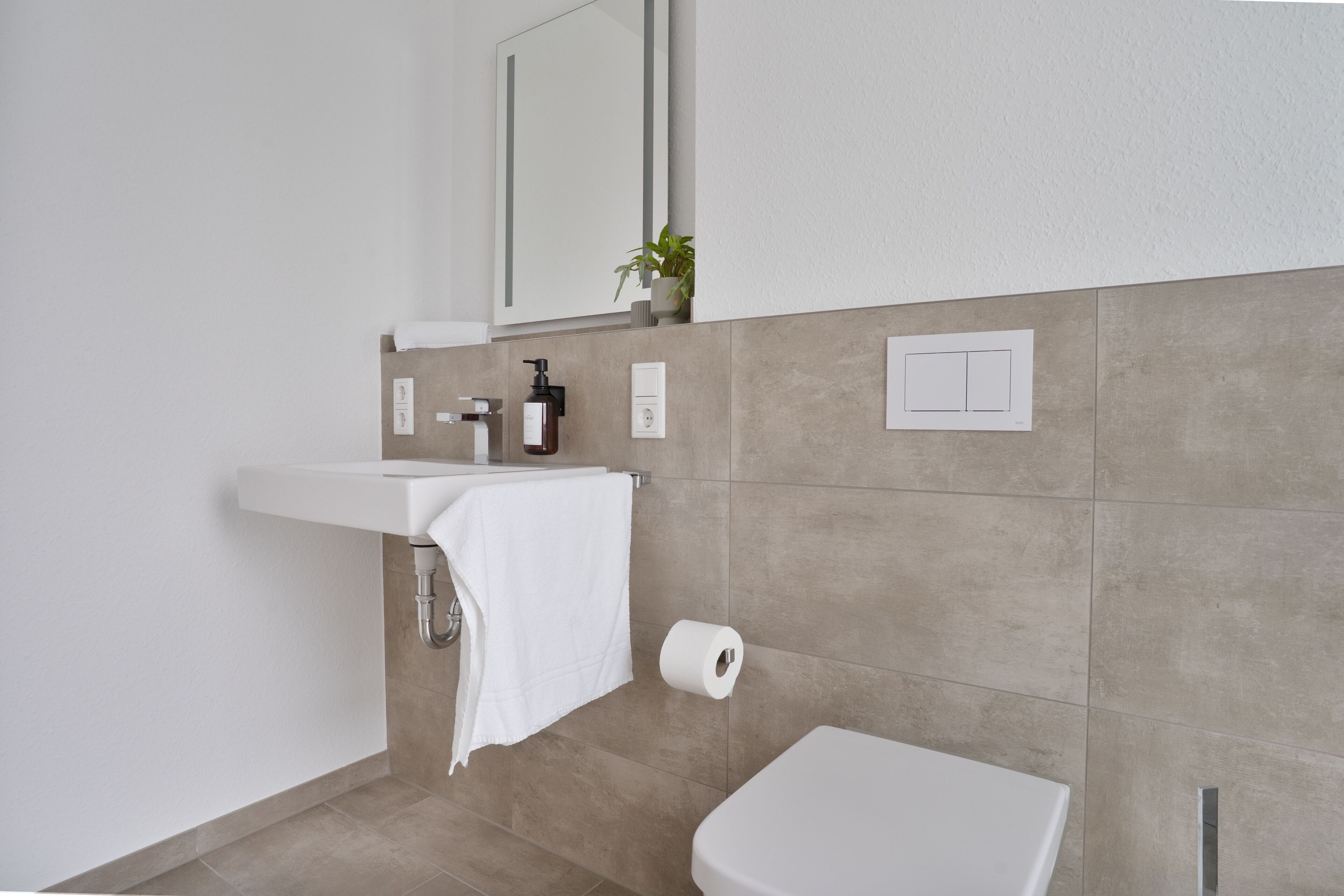 A modern bathroom with a white sink, a toilet, and a mirror above the sink.