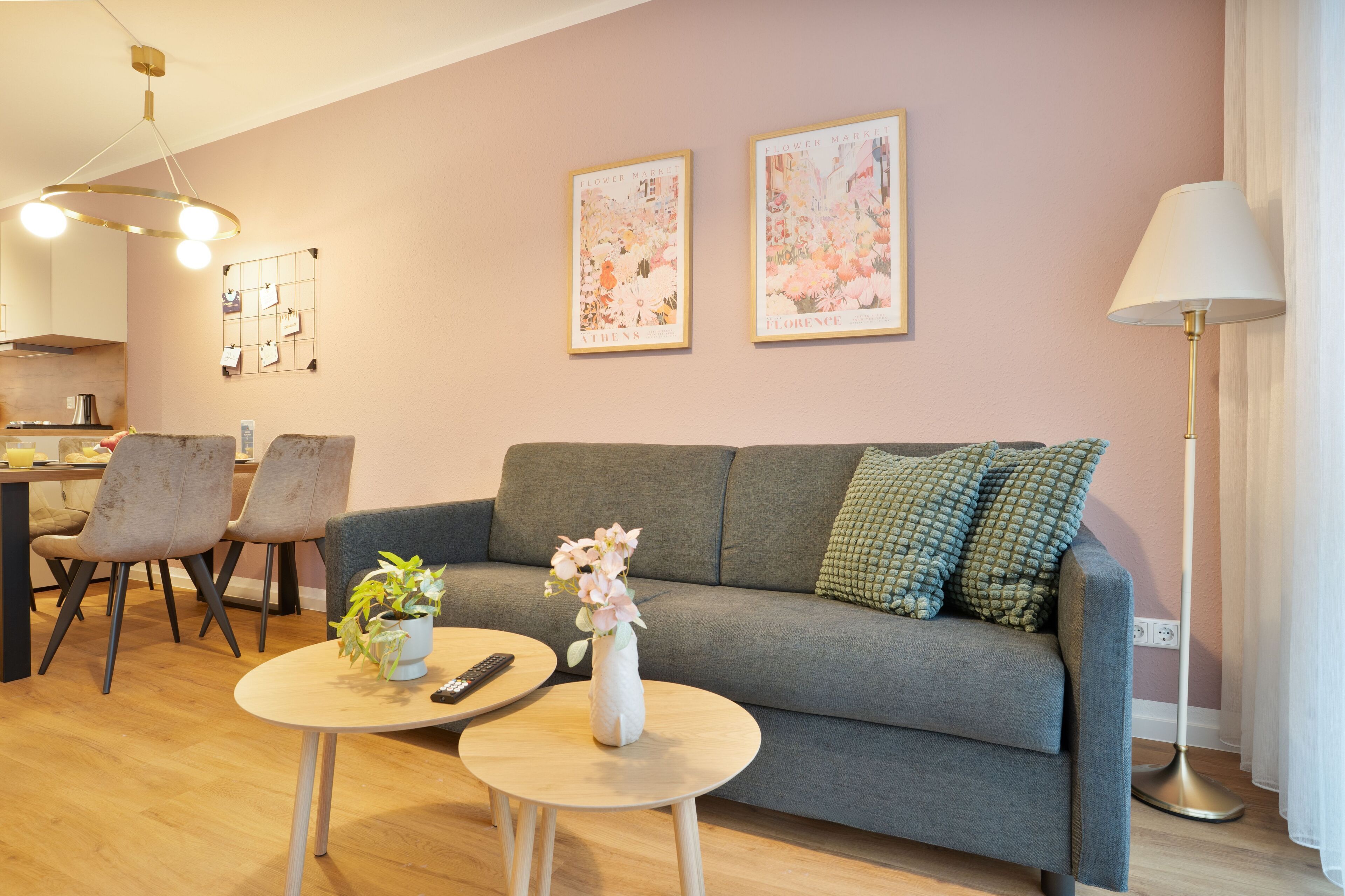 Un soggiorno moderno con un divano grigio, due tavolini rotondi, un vaso con fiori e una lampada. Alle pareti si vedono quadri incorniciati e, sullo sfondo, una zona pranzo.