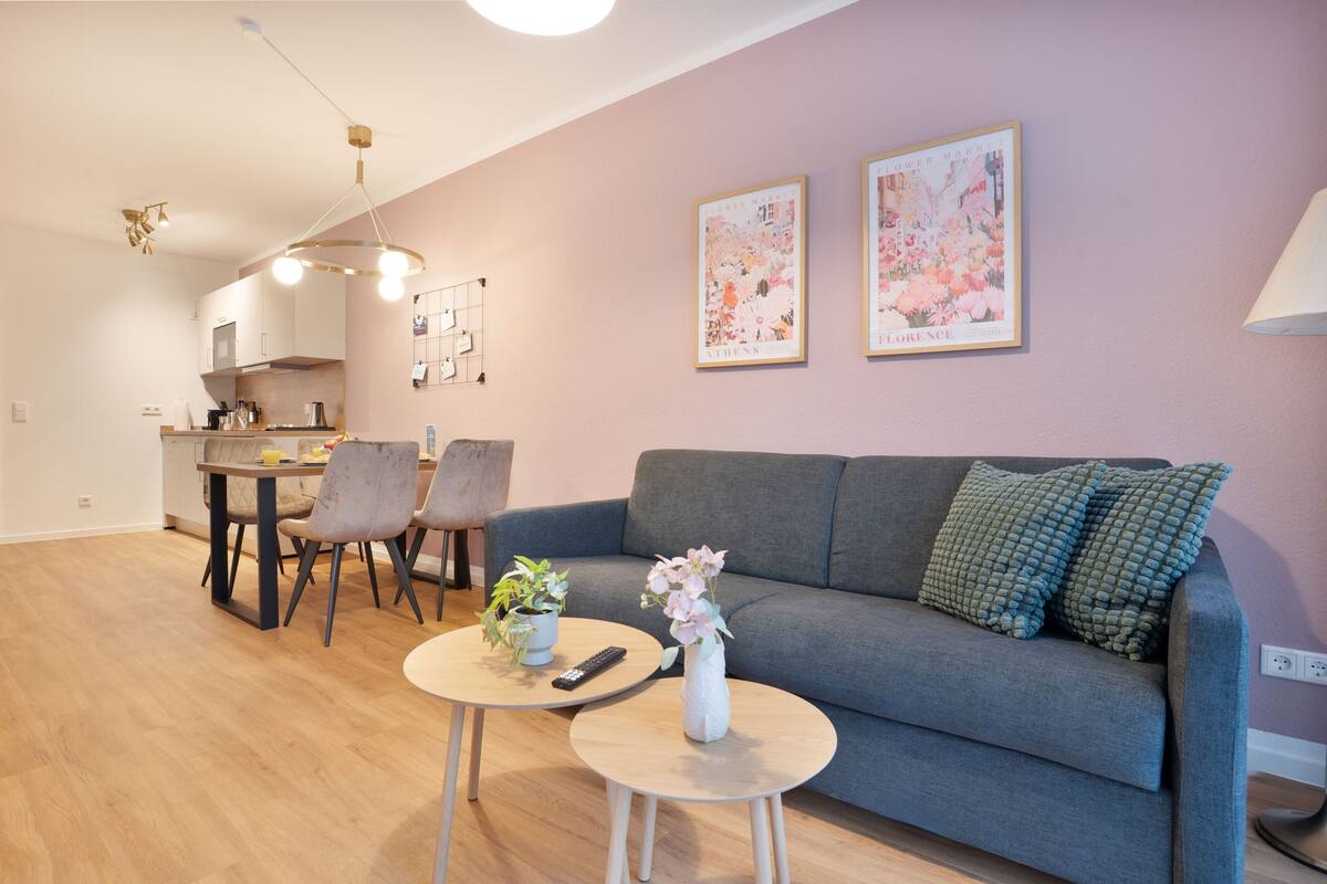 A modern living room with a grey sofa, two round coffee tables, and a dining area with a table and chairs.