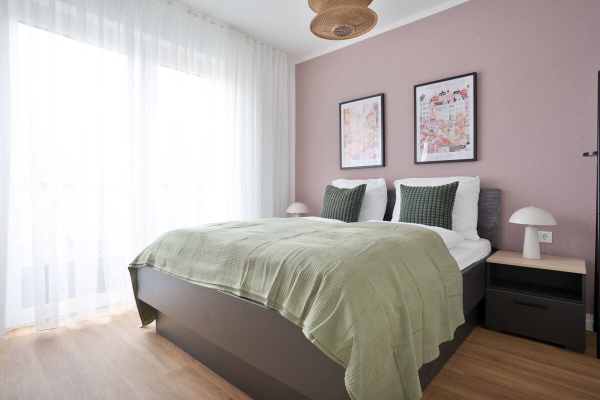A bedroom with a bed, two pillows, a bedside table with a lamp, and two framed pictures on the wall.