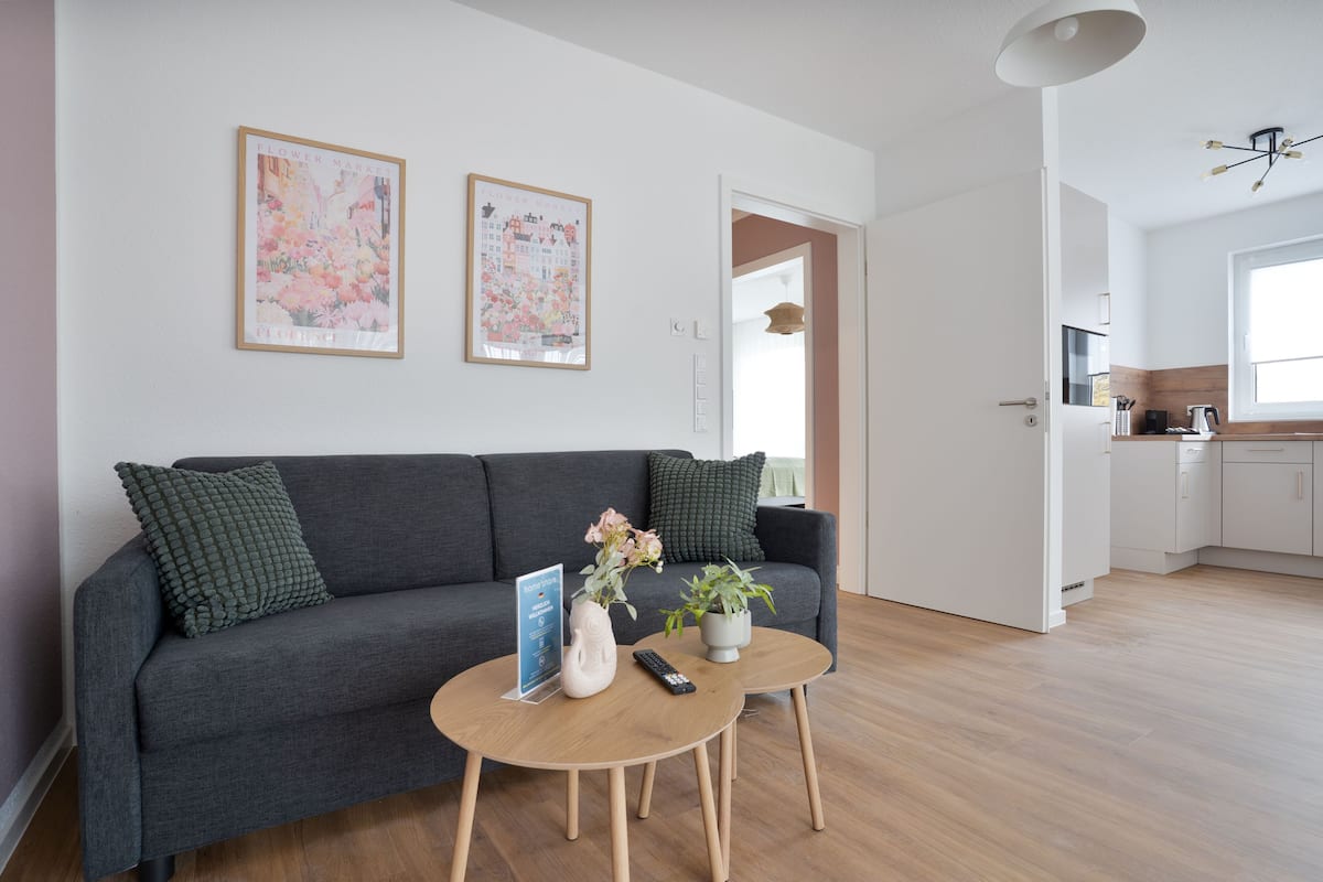 A modern living room with a grey sofa, two side tables, a vase with flowers, and framed artwork on the wall.