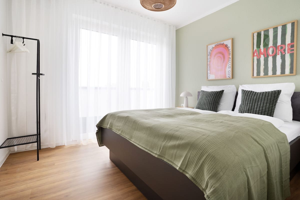 A bedroom with a bed, a hanging light, and two wall art pieces.