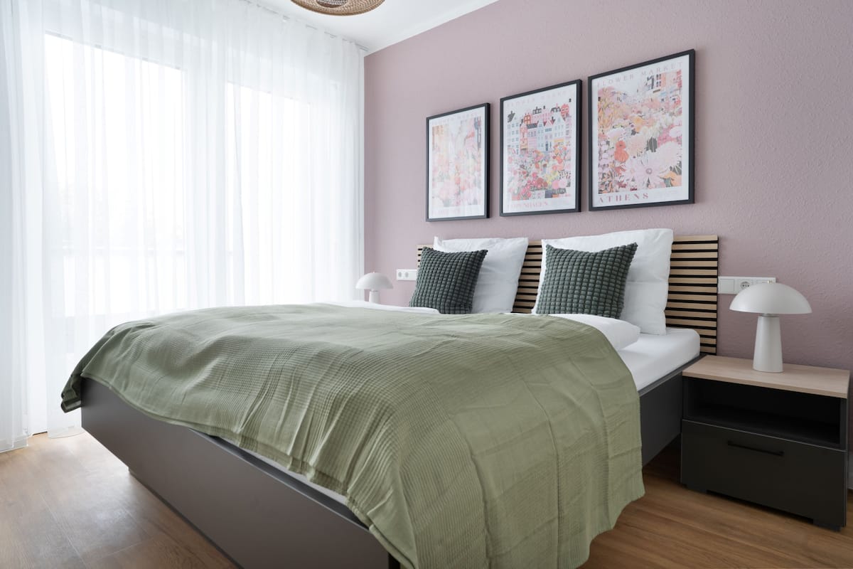 A modern bedroom with a large bed, a bedside table, and a nightstand. There are three framed artworks on the wall above the bed.