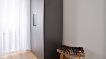 Ein Eckbereich eines Raumes mit Holzboden, einem schwarzen Kleiderschrank, einer weißen Wand und einem kleinen Holzschemel.