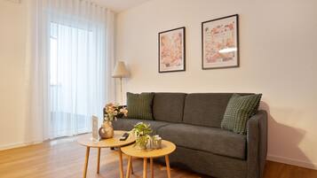 Ein Wohnzimmer mit grauem Sofa, zwei kleinen runden Tischen, einer Lampe und zwei gerahmten Bildern an der Wand.