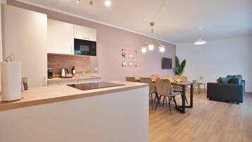 Una cocina moderna con una isla central, comedor con sillas y mesa, y zona de estar con sofá y televisor.