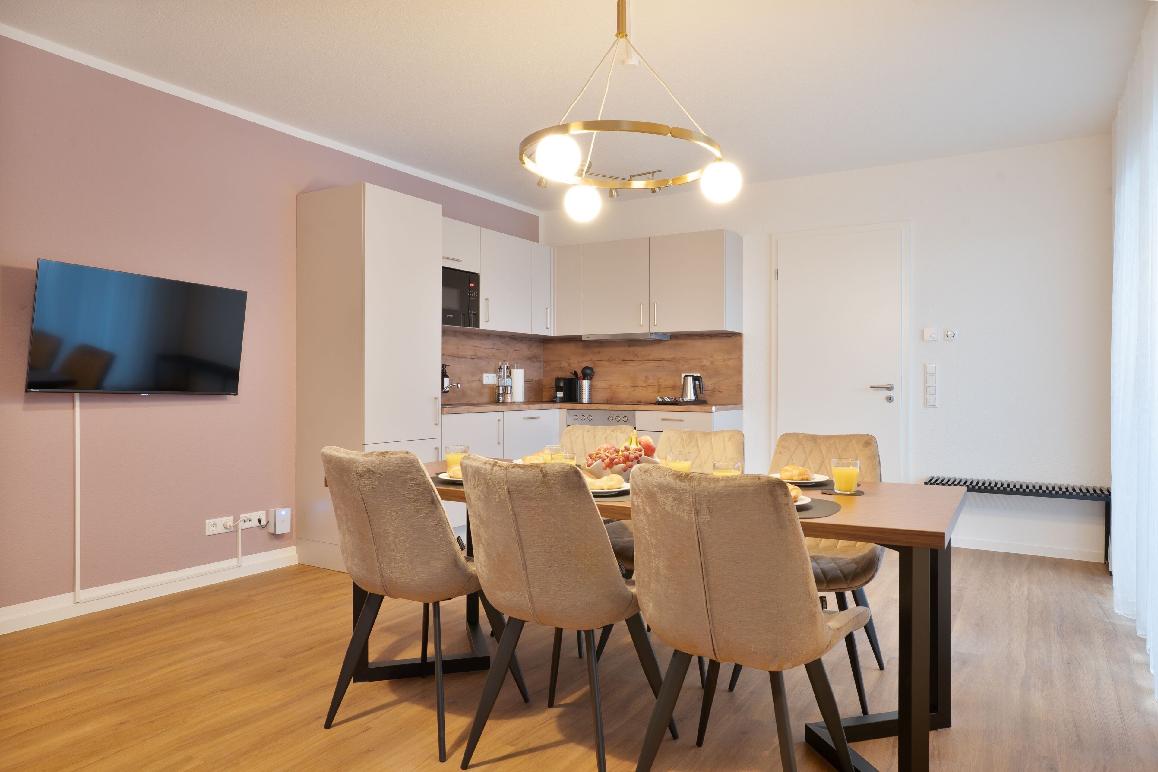 A modern dining area with a wooden table, four chairs, and a contemporary chandelier.