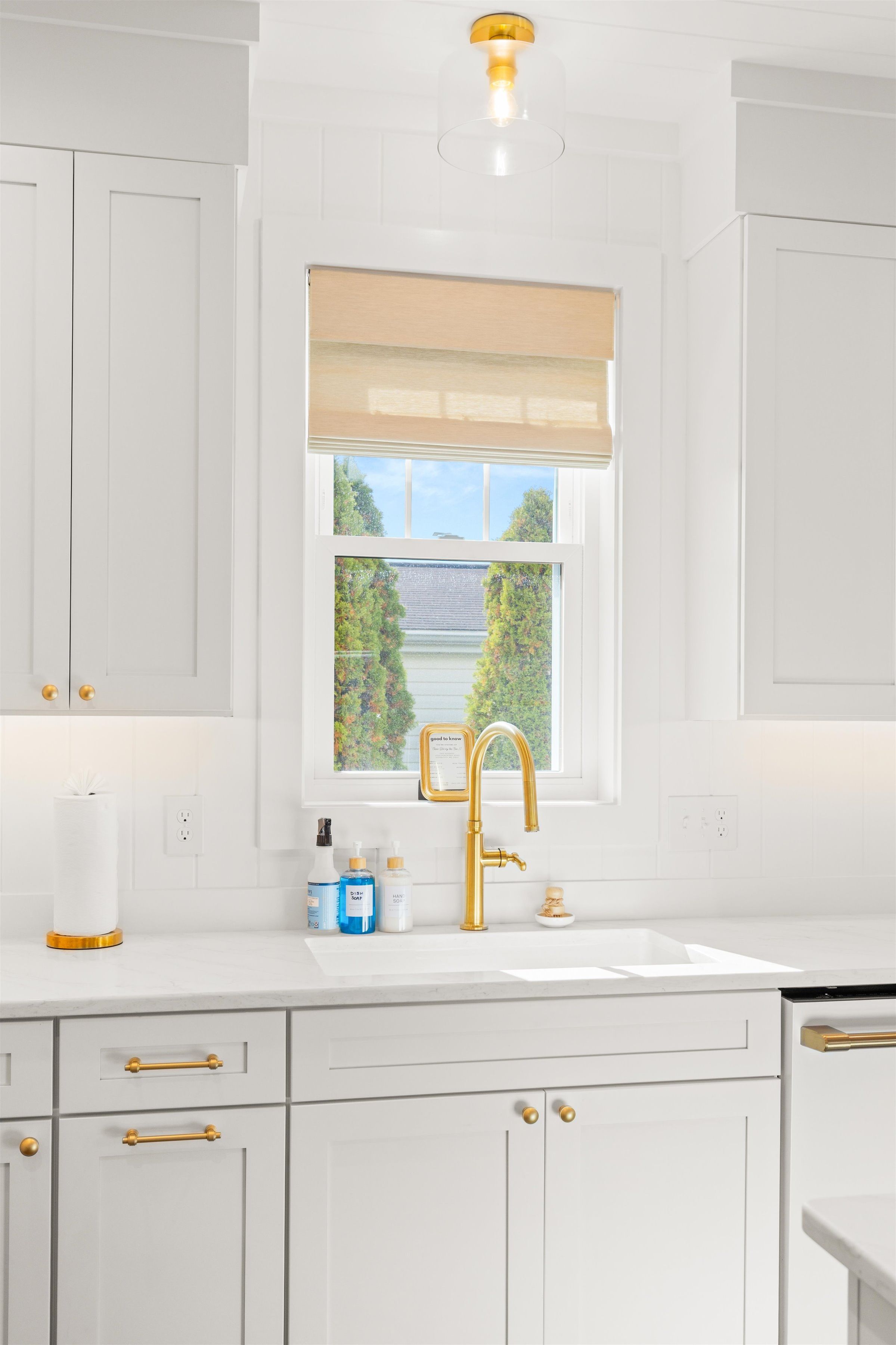 A kitchen with white cabinets, a gold faucet, and a window with a view of greenery.
