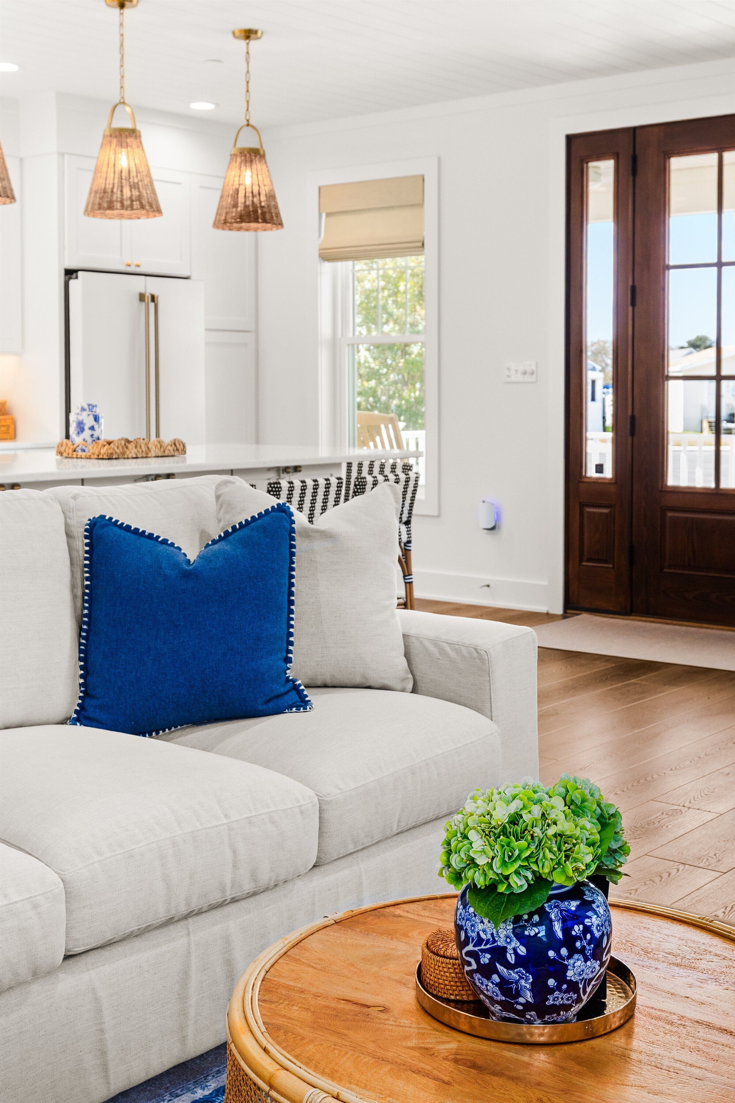 Un salon moderne avec un canapé blanc, une table basse ronde en bois et un vase bleu contenant des feuilles vertes.