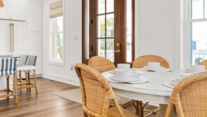 Ein Essbereich mit einem weißen Tisch, Korbstühlen und einer Holztür mit Glaseinsätzen.