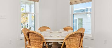 Un coin repas avec une table ronde, quatre chaises en osier et des rideaux beiges.
