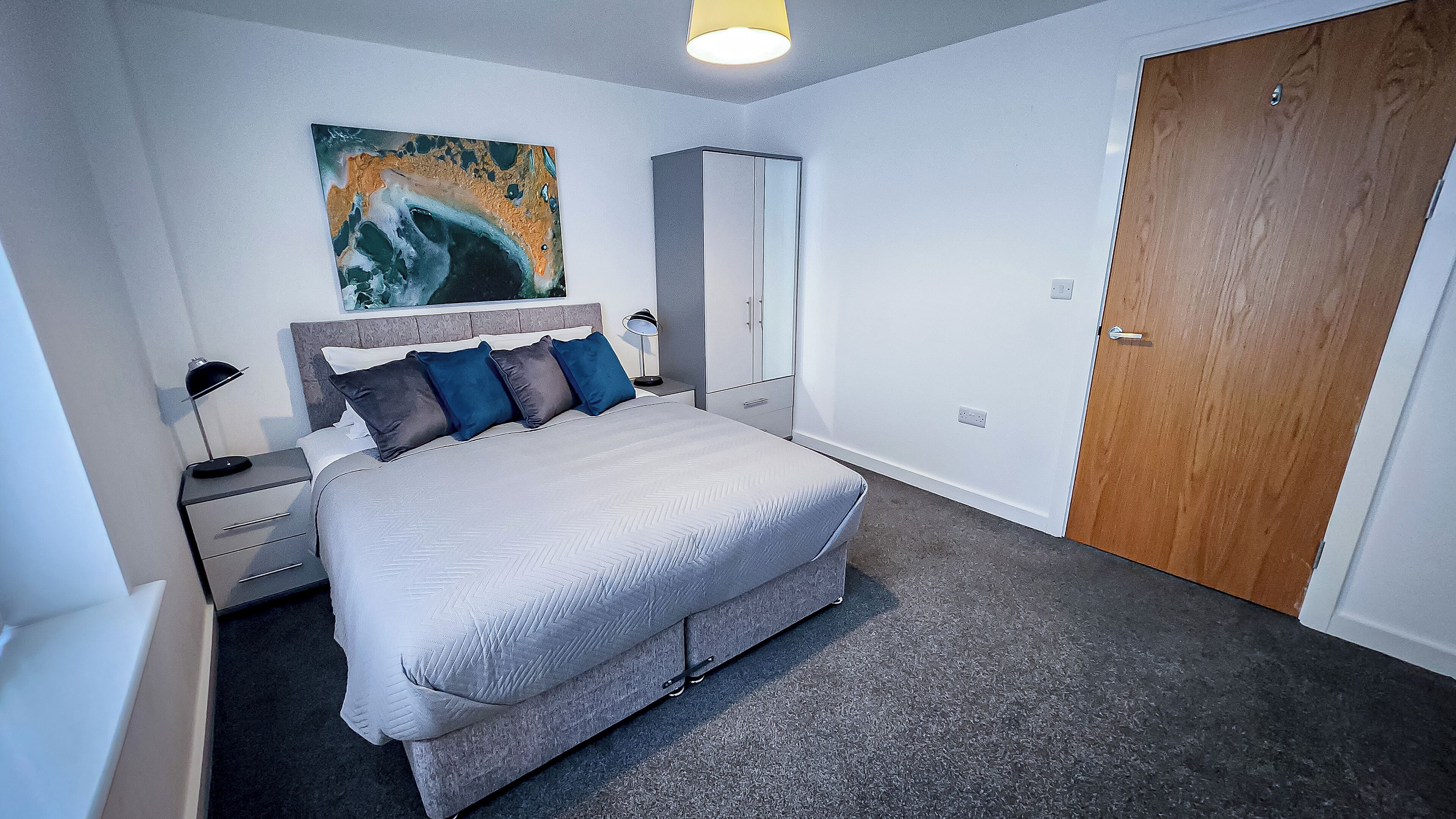 A bedroom with a bed, bedside tables, a wardrobe, a door, and a painting on the wall.