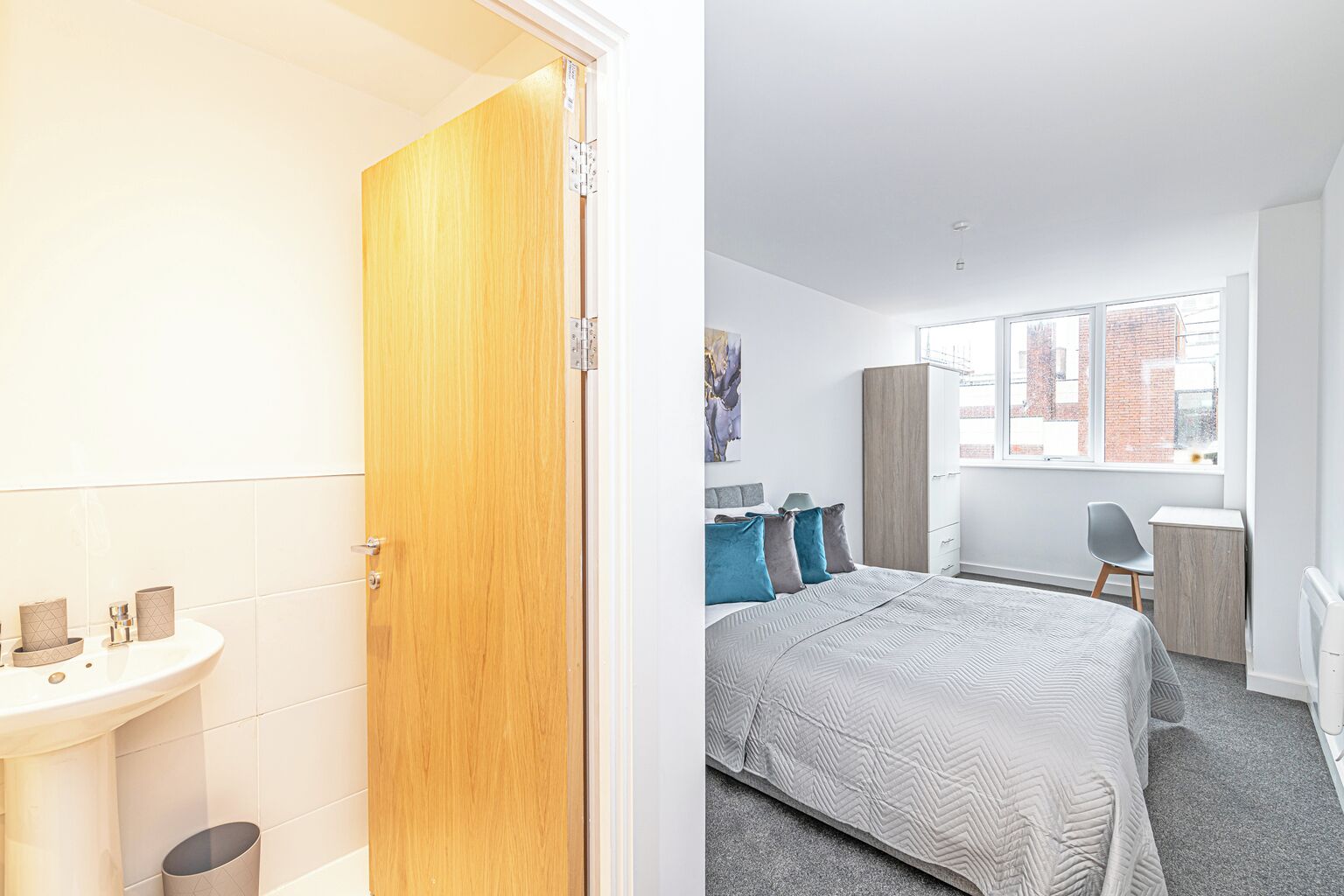 Ein modernes Schlafzimmer mit einem großen Bett, einem Schreibtisch und einem Fenster mit Blick auf Gebäude.