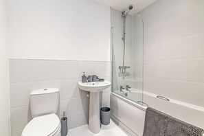 Moderni kylpyhuone, jossa on wc, pesuallas ja lasiseinällä varustettu suihku.
