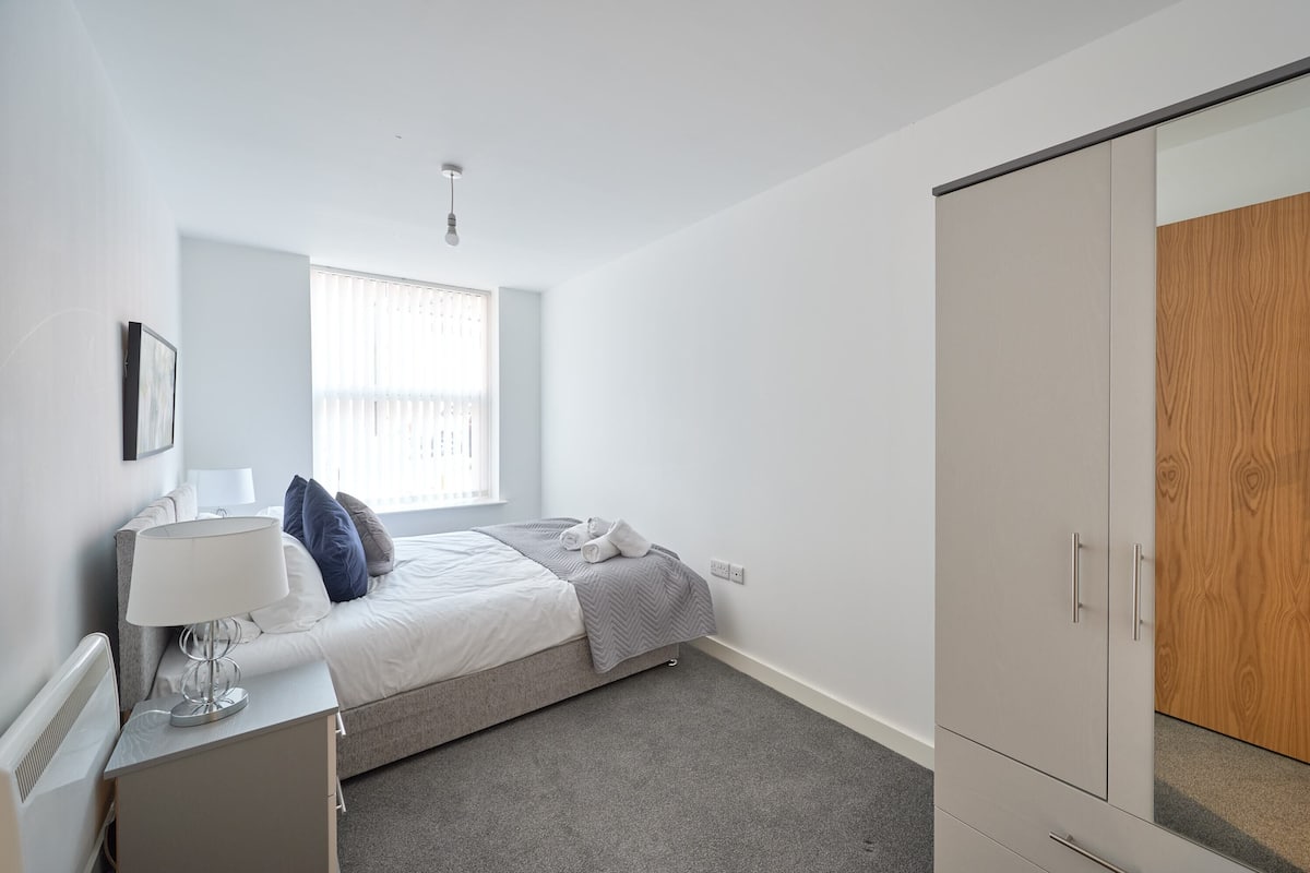A bedroom with a bed, bedside table, lamp, and wardrobe.
