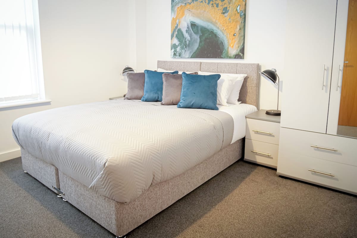 A modern bedroom with a large bed, a headboard, bedside tables, and a wardrobe.