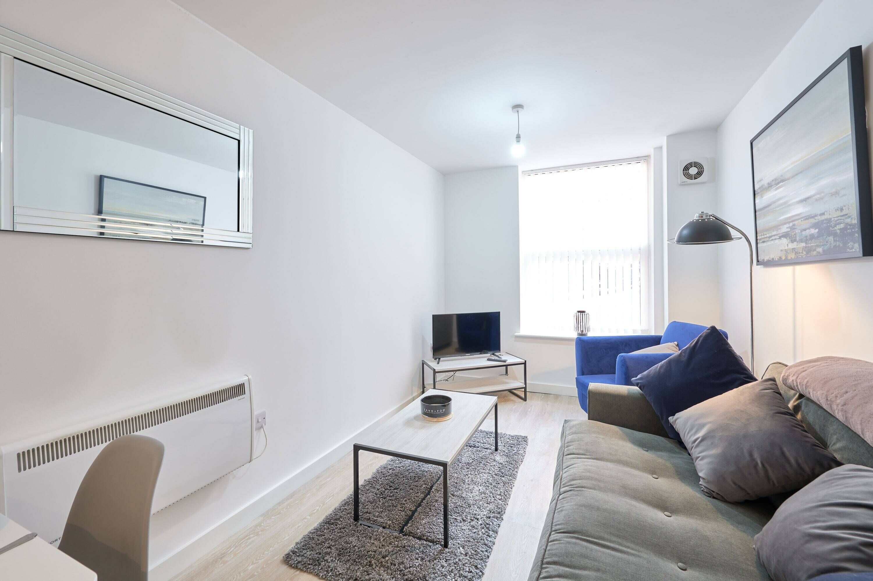A modern living room with a sofa, a coffee table, a TV on a stand, and a large window with blinds.