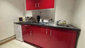 A compact kitchen with red cabinets, a small refrigerator, a microwave, a coffee maker, and a sink with a dish rack. - Petit rez-de-chaussée du théâtre (Arras)