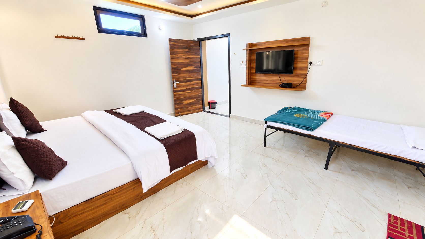 Habitació d'hotel amb un llit, una banca, un televisor i un penjador.