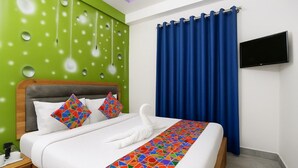 Habitación de hotel con una cama, una pared verde con diseños circulares, una cortina azul y un televisor de pantalla plana.