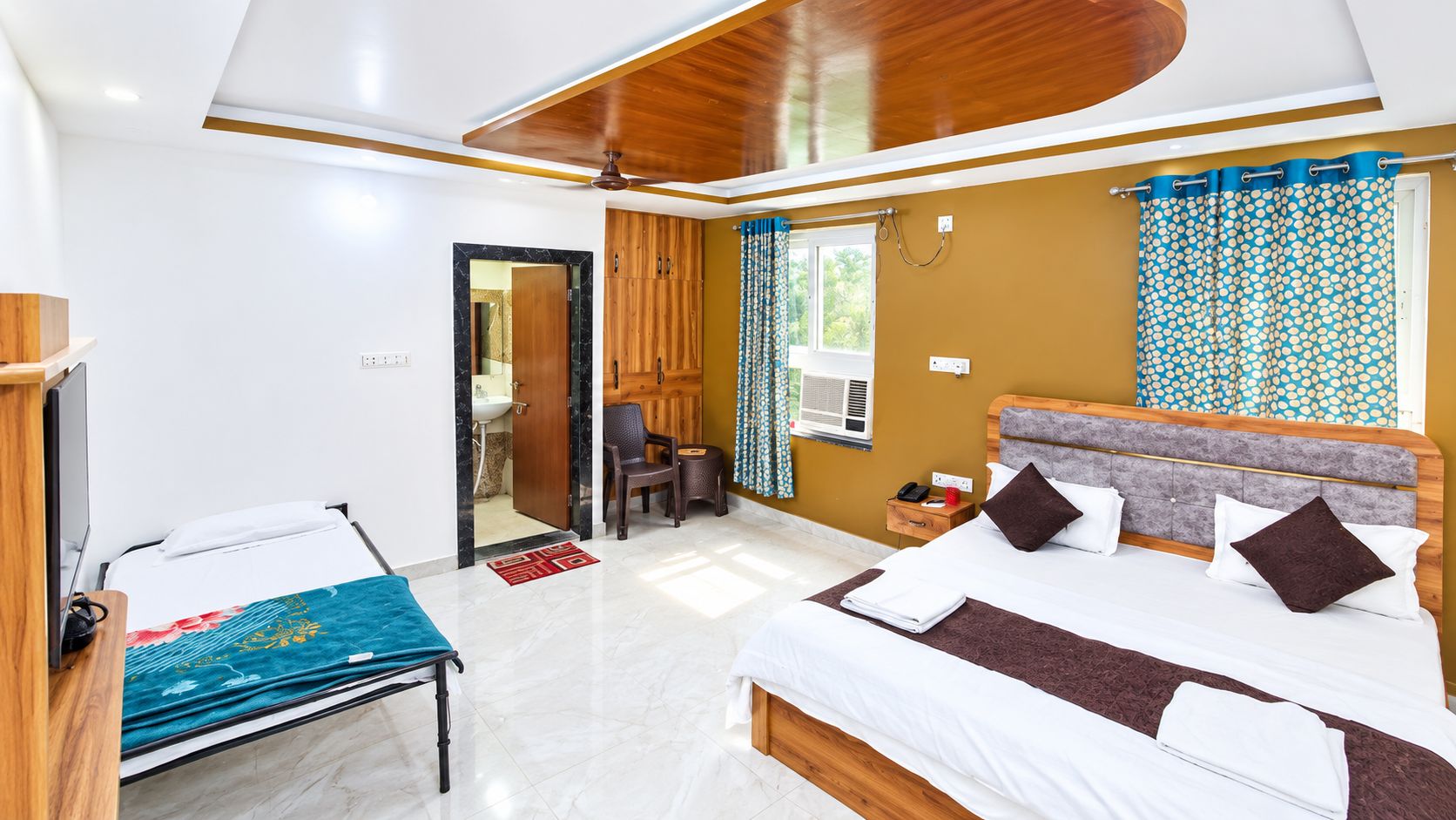 Habitación de hotel con cama, escritorio, silla, armario y baño visible a través de una puerta abierta.