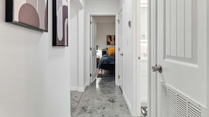 A narrow hallway with a bed at the end, white walls, and a gray floor.