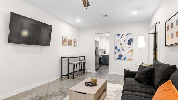 A modern living room with a flat-screen TV, a dark grey sofa, a wooden coffee table, and a ceiling fan.