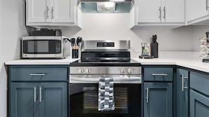 A modern kitchen with white cabinets, a stainless steel stove, and a microwave.