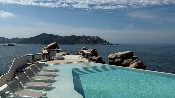 A pool with lounge chairs and a view of the sea and a distant island.