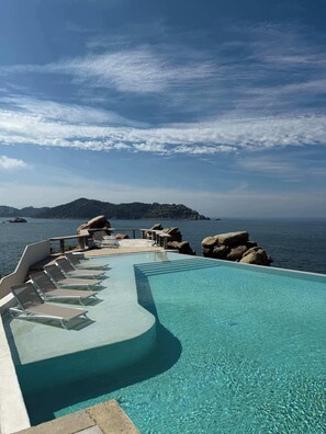 Una piscina con lettini e vista sul mare e un'isola in lontananza.