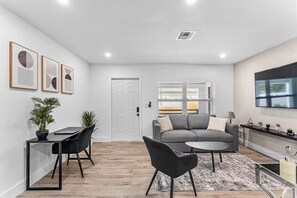 Una sala de estar moderna con un sofá gris, una mesa de comedor con sillas y un televisor montado en la pared.