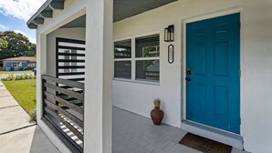 Ein Haus mit blauer Tür, weißem Anstrich und einer kleinen Veranda mit Holzgeländer.