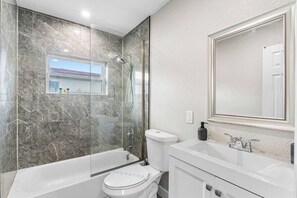 Un baño moderno con ducha de vidrio, inodoro y lavamanos con espejo.