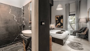 Un baño moderno con un lavabo grande, ducha y una cama en la habitación contigua.