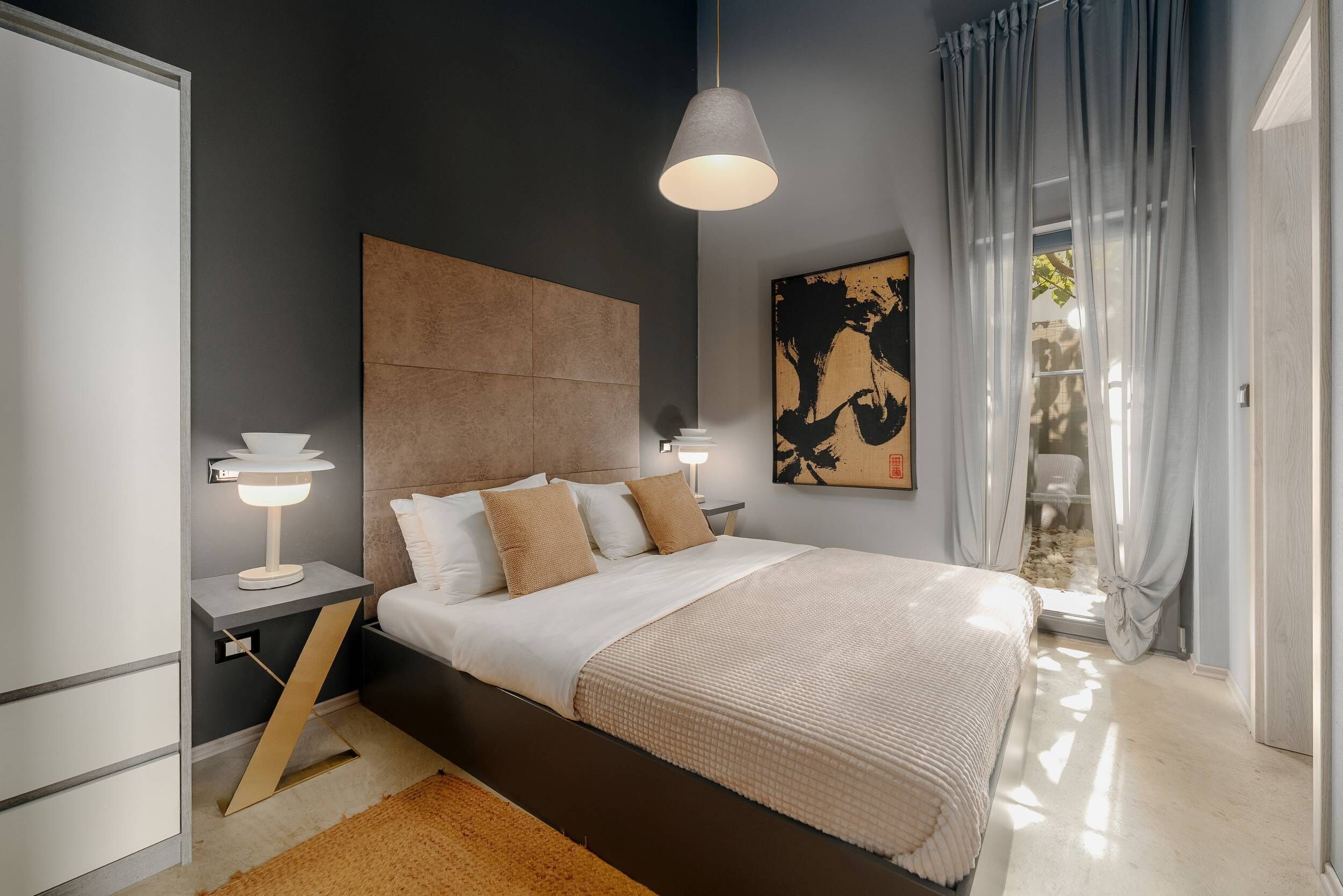 A modern bedroom with a large bed, bedside lamps, a headboard, and a painting on the wall.