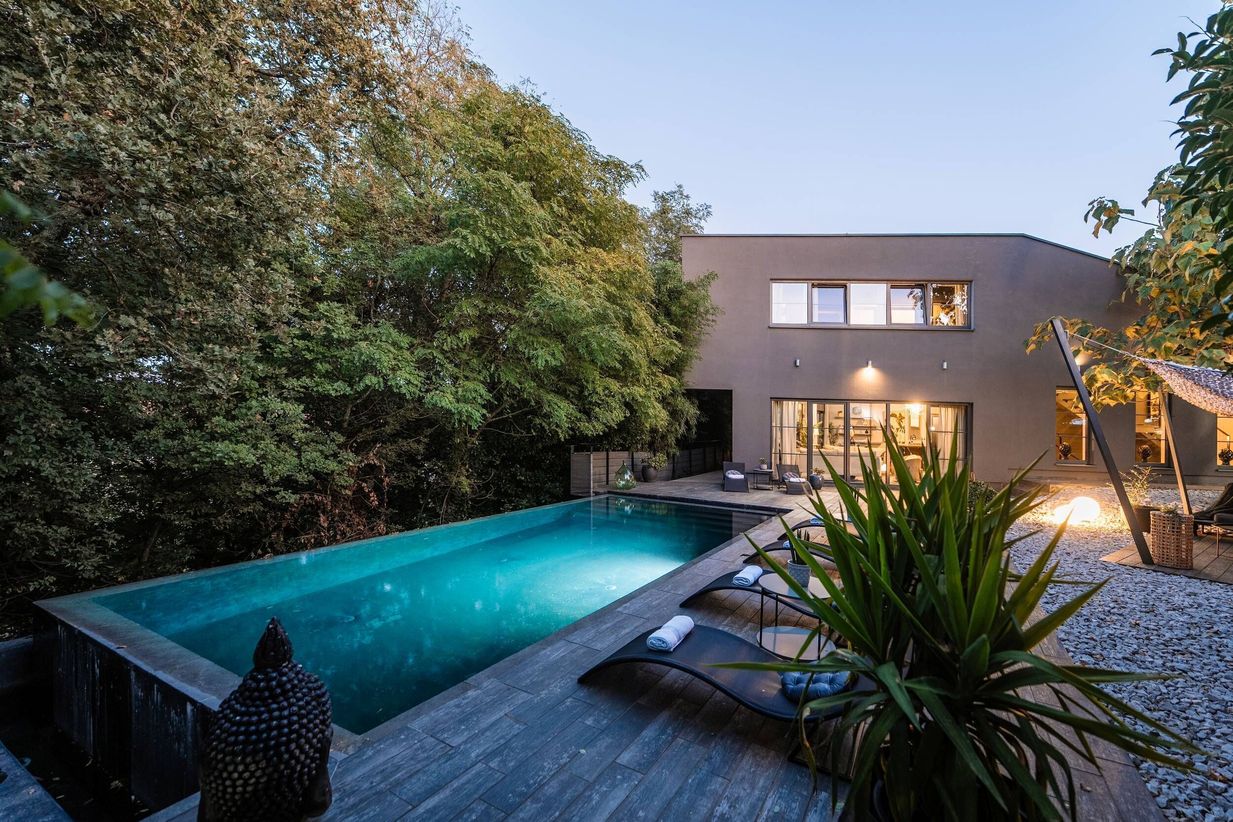 A modern house with a swimming pool, a deck with lounge chairs, and a well-maintained garden.